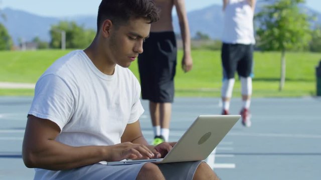 Teen basketball player using laptop computer at outdoor court