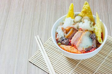 Pink seafood flat noodles (Tom Yum Yen-Ta-Fo) with fish ball and dumpling fish, special homemade red sauce serve in white bowl on wooden table