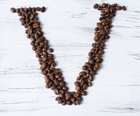 V letter of the English alphabet made of coffee beans. Light, old wooden background. Selective focus.