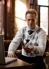 Psychiatrist man smiling for camera and holding hourglass in hand while waiting for patients in his office. Portrait of handsome psychiatrist man looking at camera.