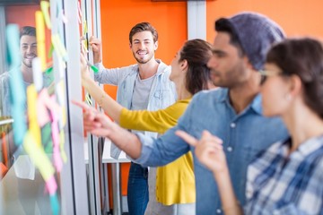 Obraz premium Smiling executives reading sticky notes on glass wall