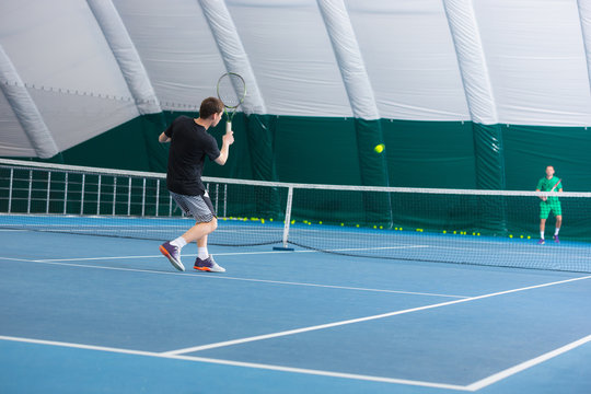 The young man in a closed tennis court with ball