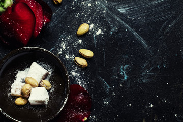 Oriental sweets with almonds and pink petals, dark background, flat lay