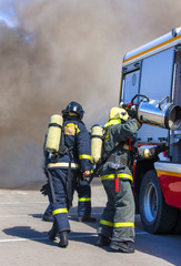 Team firefighters extinguish a fire in the smoke with the help of a fire engine.