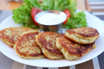 Potato pancakes served on plate with sour cream and salad leaves