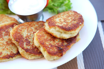 Potato pancakes served on plate with sour cream and salad leaves
