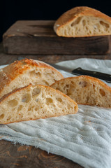 Whole and slices of freshly baked sourdough bread on a white napkin. Wooden background. Close up. Rustic style.