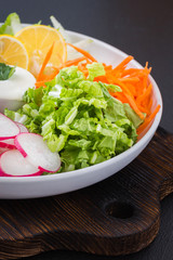Fresh vegetable salad on a white plate with sauce. Summer salad. Light healthy snack. Clean eating. Raw vegetables and yogurt dressing in a white plate on wooden board.