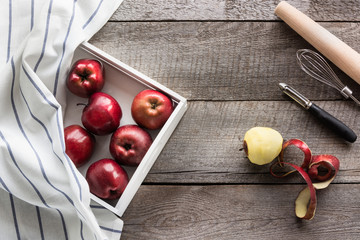 Ripe red apples in white birch tray with napkin on wooden board, accessories for baking and copy space for your text.