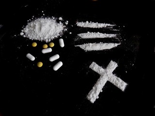 Cocaine drug powder, lines and cross and pills on black background
