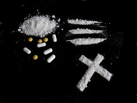Cocaine drug powder, lines and cross and pills on black background