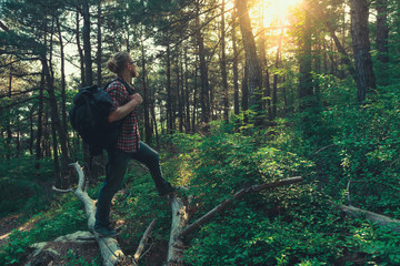 Tourist man with  backpack walks through the forest and enjoys the view of the sun. Concept of adventure, hiking and discovery