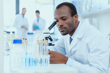 African american scientist in white coat working with microscope in laboratory, laboratory researcher concept