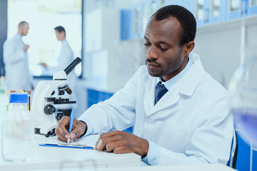 African american scientist in white coat taking notes while working in laboratory, laboratory researcher concept