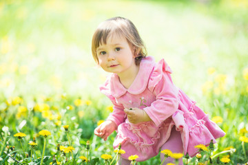 Girl in pink dress with dandelion on green grass.