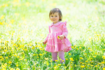 Girl in pink dress with dandelion on green grass.