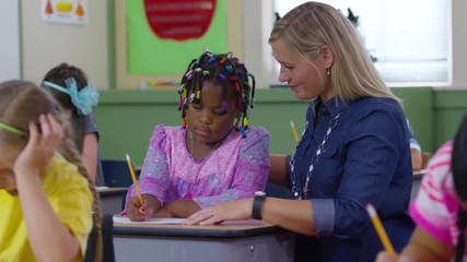 Teacher helps student with writing project in school classroom