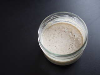 Homemade sourdough starter in glass jar, isolated on black background