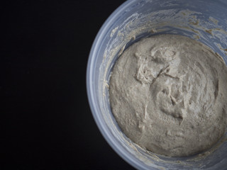 Homemade dough rising in plastic bowl, on black background
