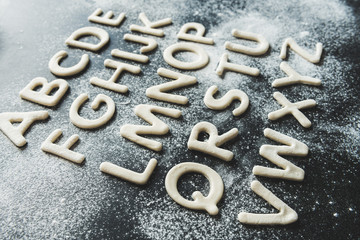 Close up of dough for cookies in forms of letters with powdered sugar, cookie dough