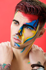 portrait of young man with colored face paint on red background. Professional Makeup Fashion. fantasy art makeup