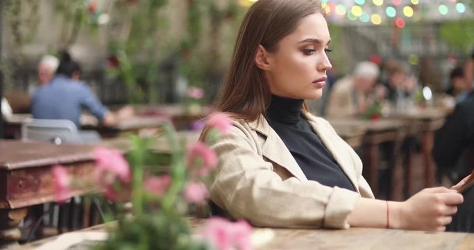 Side view of young woman in coat sitting at table with menu and looking it through making choice