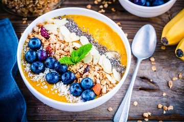 Yellow smoothies bowl with blueberries, granola, chia seeds and almonds