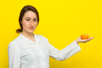 Young female nutritionist with half citrus in her hand on yellow background