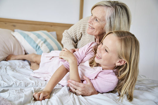 Little girl lying on the bed with her grandmother having fun