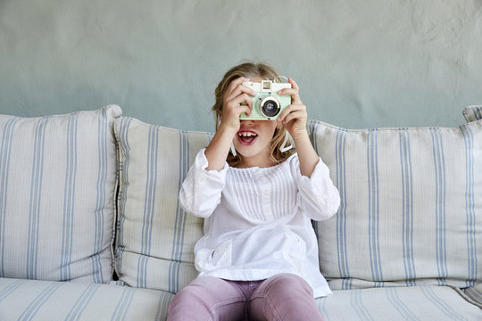 Portrait of smiling little girl sitting on couch taking picture with camera