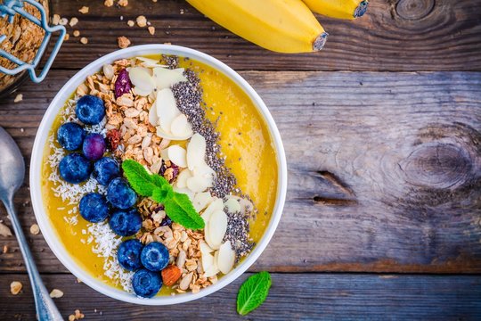 Yellow smoothies bowl with blueberries, granola, chia seeds and almonds