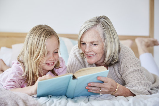 Little girl lying on the bed with her grandmother reading a book