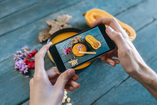 Close-up of man's hands taking picture of creamed pumpkin soup with smartphone
