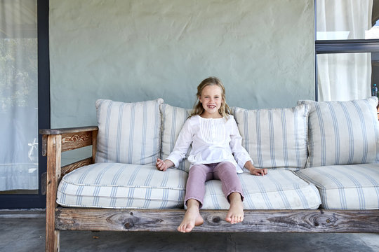 Portrait of smiling blond little girl sitting on couch on the terrace