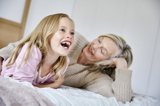 Portrait of laughing little girl lying on the bed with her grandmother