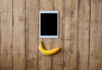 Top view of fresh ripe banana and digital tablet on wooden surface