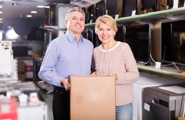 smiling mature married couple in shop packed household appliances into boxes