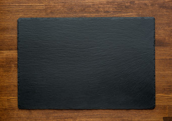 Black slate stone on wooden background, top view