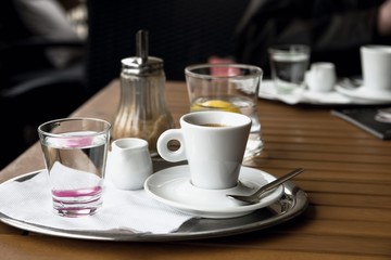 Espresso coffee, water, jug, sugar on wooden table.