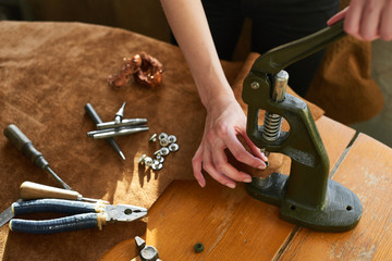 Female artisan using manual vintage machine tool for pinching buttons on leather material
