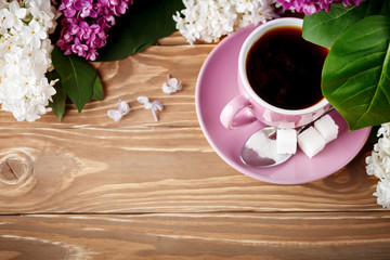 Still life with branches of lilac and a Cup of coffee on a wooden table.