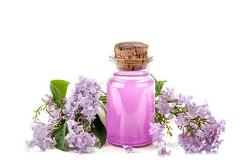 Glass bottle of lilac oil and the blooming branches of lilac on a white background.