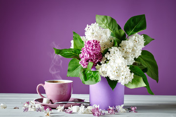 Still life with branches of lilac and a Cup of coffee on a wooden table.