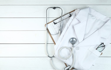 stethoscope,clipboard and doctor’s uniform on white neat wooden desk