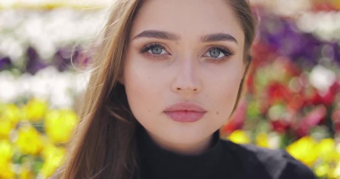 Portrait of young and beautiful woman with makeup looking at camera on blurred background of colorful flowers in spring time