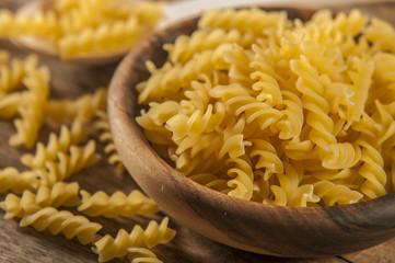 Pasta fusilli in a wooden bowl on wood background for healthy recipes.