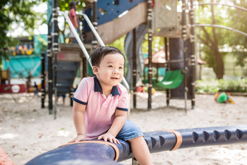 Fototapeta na wymiar Happy asian boy playing seesaw at the playground in the park