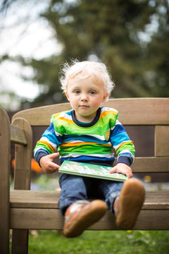 Kind sitzt mit dem Buch auf der Bank