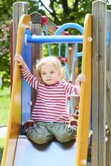 Fototapeta na wymiar Happy little toddler blond girl having fun sliding on playground