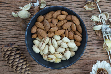 Roasted healthy delicious pistachios and almonds nuts food in black bowl on wooden table background